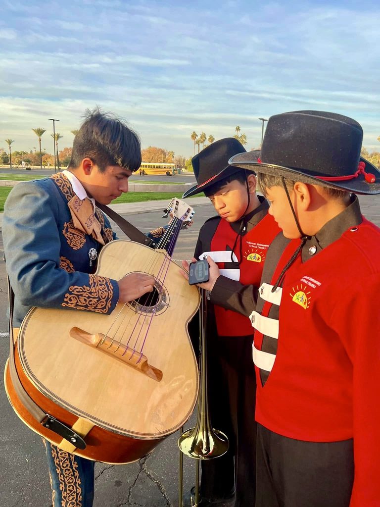 Three young boys tuning a guitar from mariachi band.